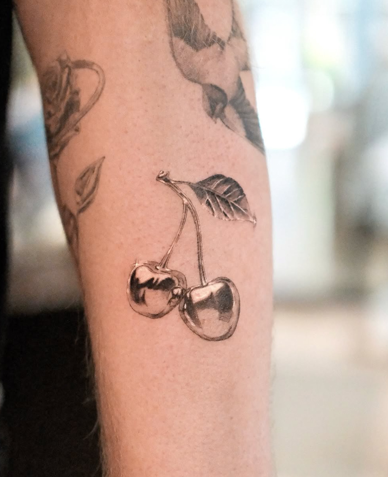 Black and grey chrome style tattoo of a cherry on white skin